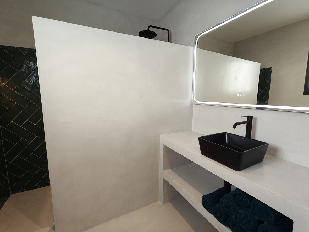 Modernes Badezimmer mit Mikrozement-Oberflächen, schwarzem Aufsatzwaschbecken und LED-Spiegel. Die begehbare Dusche besticht durch dunkelgrüne Fischgrätfliesen und schwarze Armaturen.