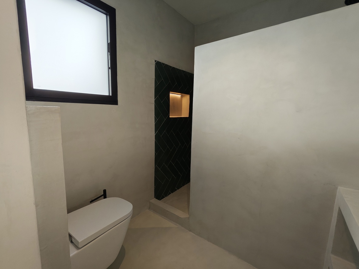 Modernes Badezimmer mit Mikrozementwänden, Wand-WC und begehbarer Dusche mit dunkelgrünen Fischgrätfliesen und einer beleuchteten Wandnische.