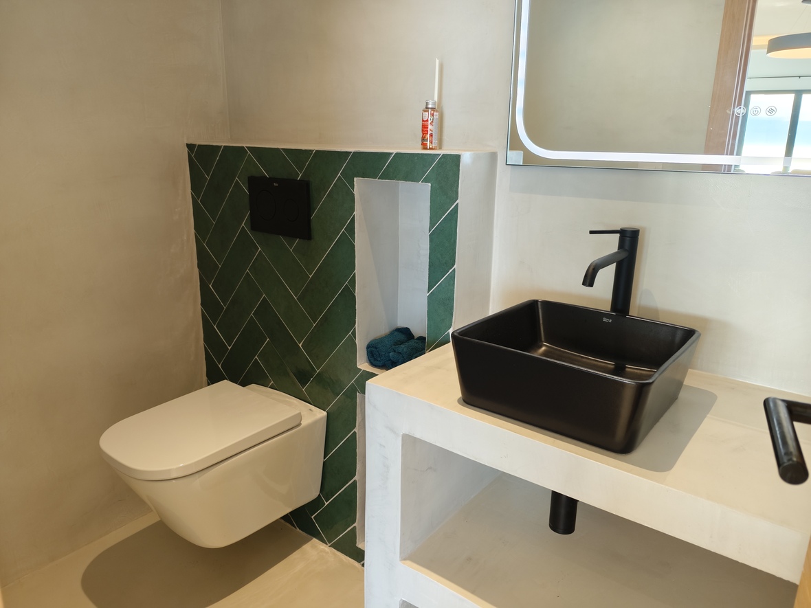 Modernes Badezimmer mit schwarzem Aufsatzwaschbecken auf einem Mikrozement-Waschtisch, grünen Fischgrätfliesen und einem wandhängenden WC.