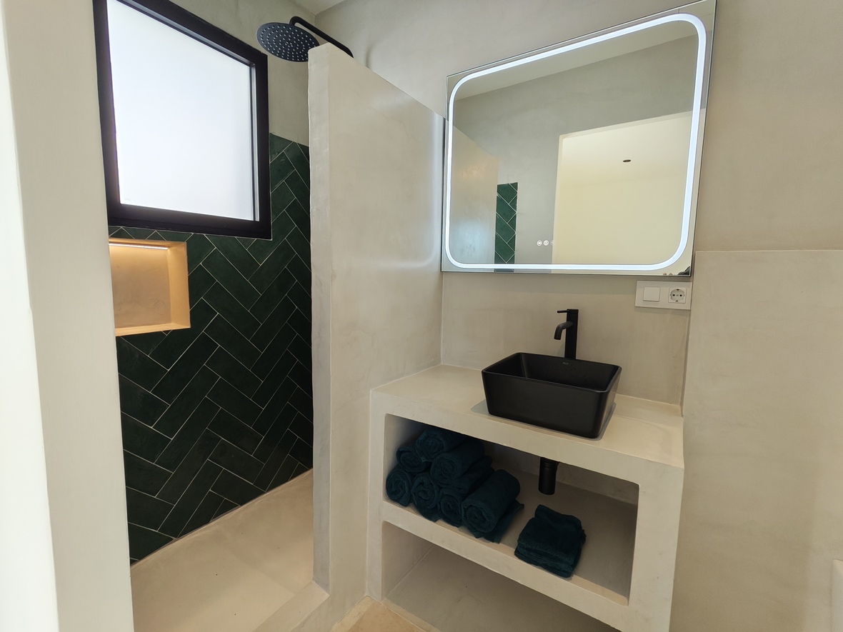 Modernes Badezimmer mit schwarzem Aufsatzwaschbecken, LED-Spiegel und begehbarer Dusche mit smaragdgrünen Fischgrätfliesen und Mikrozement-Wänden.