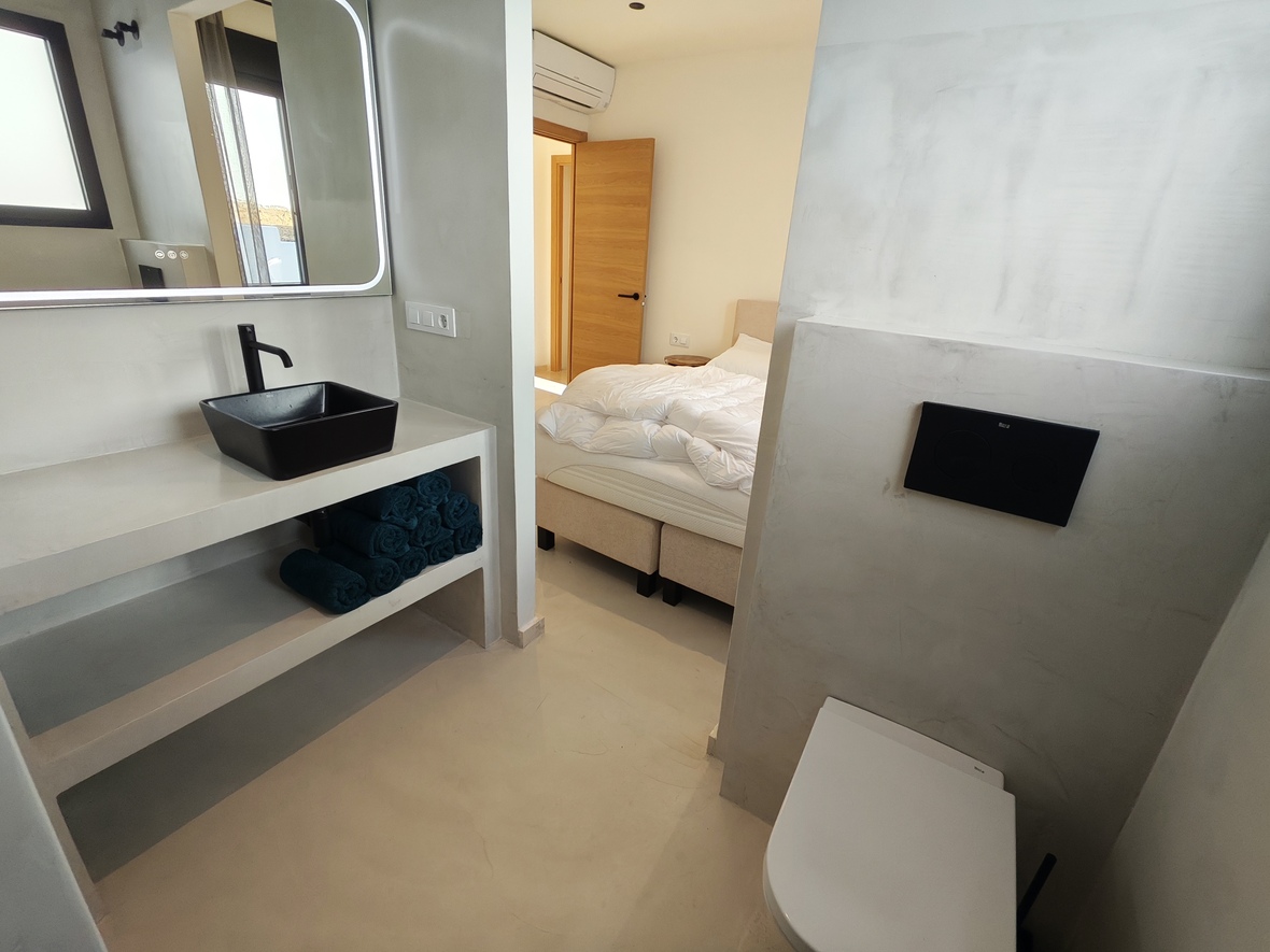 Modernes En-Suite-Badezimmer mit Mikrozement-Oberflächen, schwarzem Aufsatzwaschbecken und hintergrundbeleuchtetem Spiegel neben dem Schlafzimmer.