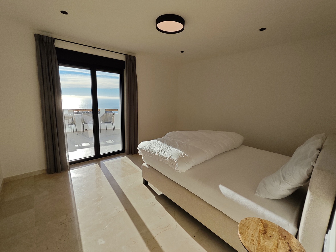 Modernes Schlafzimmer mit poliertem Marmorboden, Doppelbett und Glasschiebetüren, die auf eine Terrasse mit weitem Meerblick führen.
