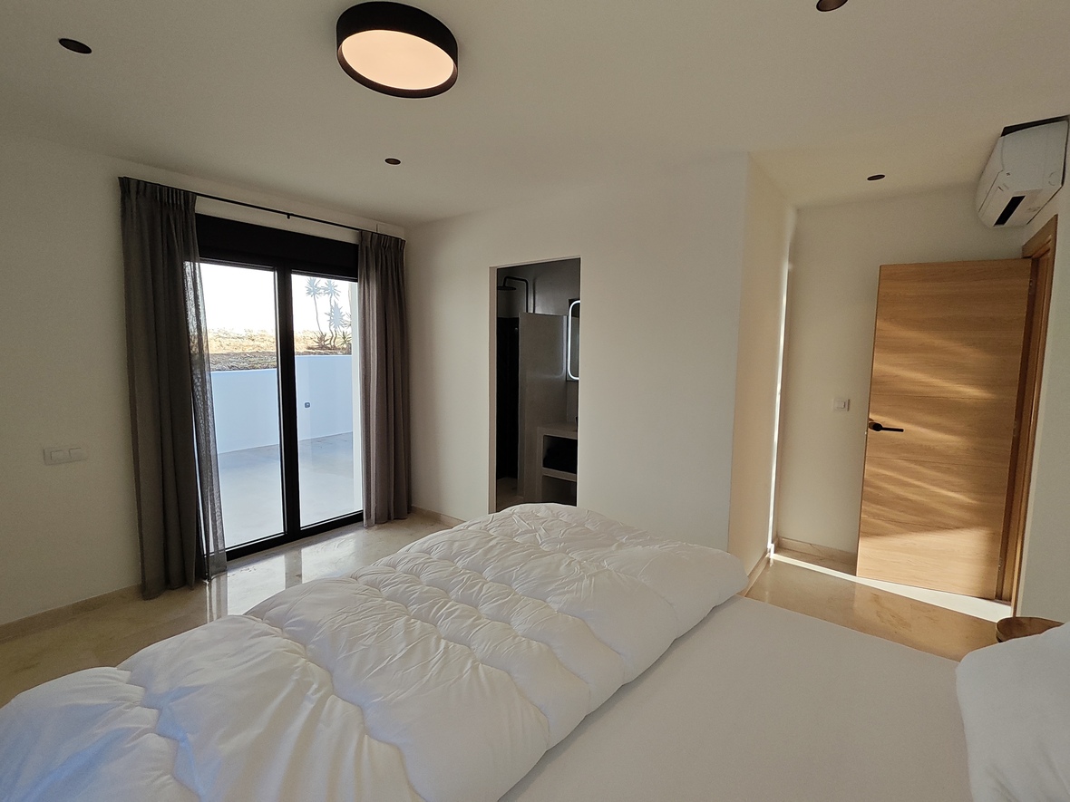 Modernes Schlafzimmer mit poliertem Steinboden, direktem Terrassenzugang und integriertem En-Suite-Badezimmer im minimalistischen Stil.