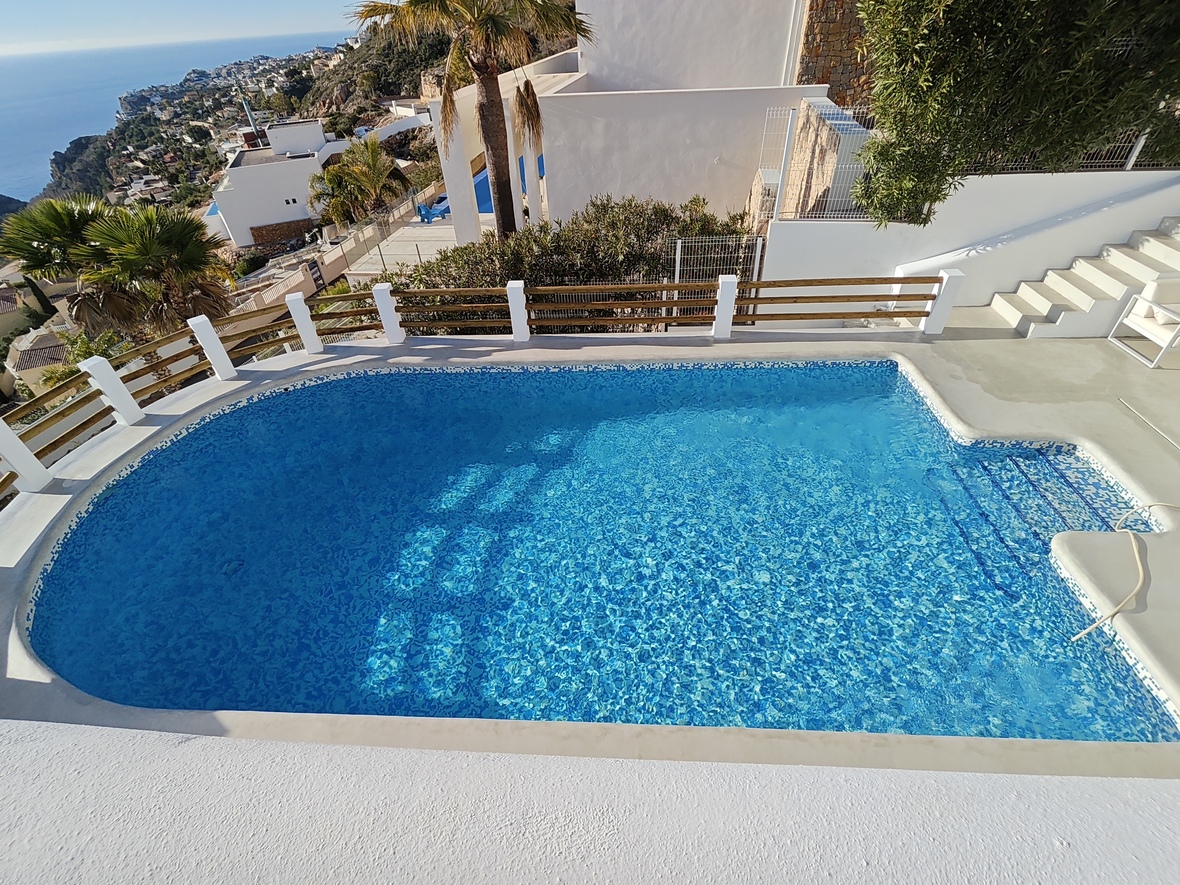 Privater Mosaikpool mit integrierter Treppe, umgeben von einer weißen Terrasse und Holzgeländer mit weitem Blick über die mediterrane Küstenlandschaft.