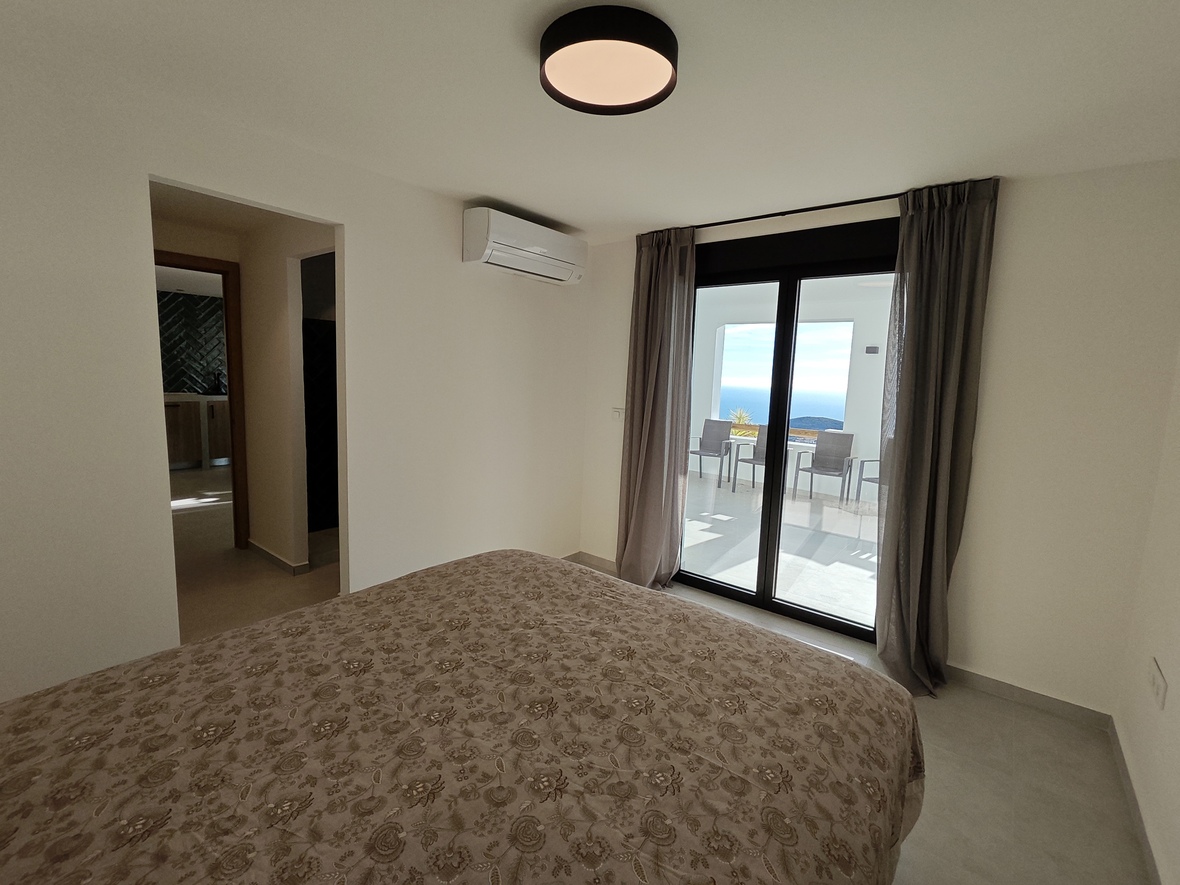 Schlafzimmer mit direktem Zugang zu einer Terrasse mit Meerblick. Ausgestattet mit Klimaanlage, neutralem Dekor und großen Glasschiebetüren mit grauen Vorhängen.