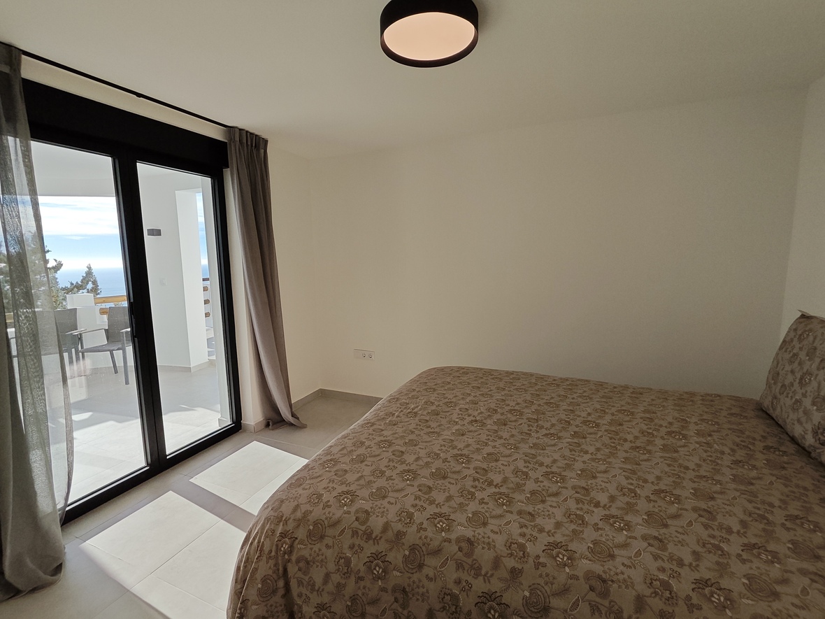 Schlafzimmer mit Doppelbett, floraler Bettwäsche und direktem Zugang zur privaten Terrasse mit Meerblick durch große Glasschiebetüren.