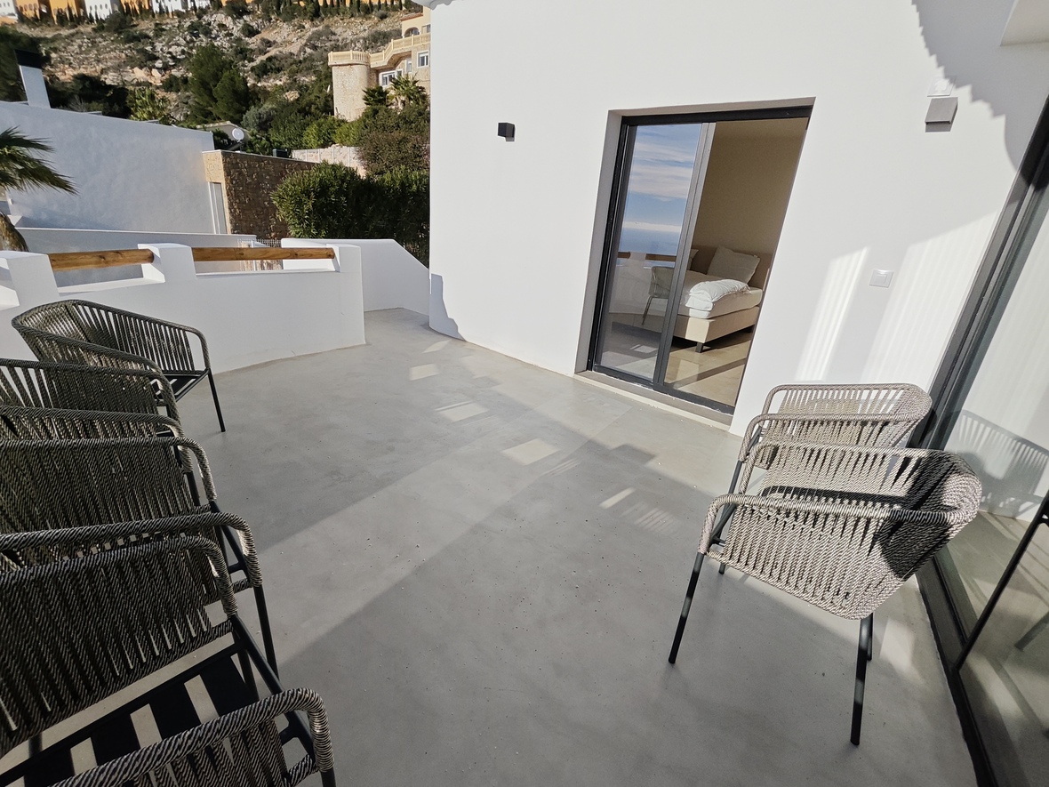Terrasse mit glattem Betonboden und modernen Sesseln aus Seilgeflecht, die einen direkten Zugang zum Schlafzimmer durch Glasschiebetüren bietet.