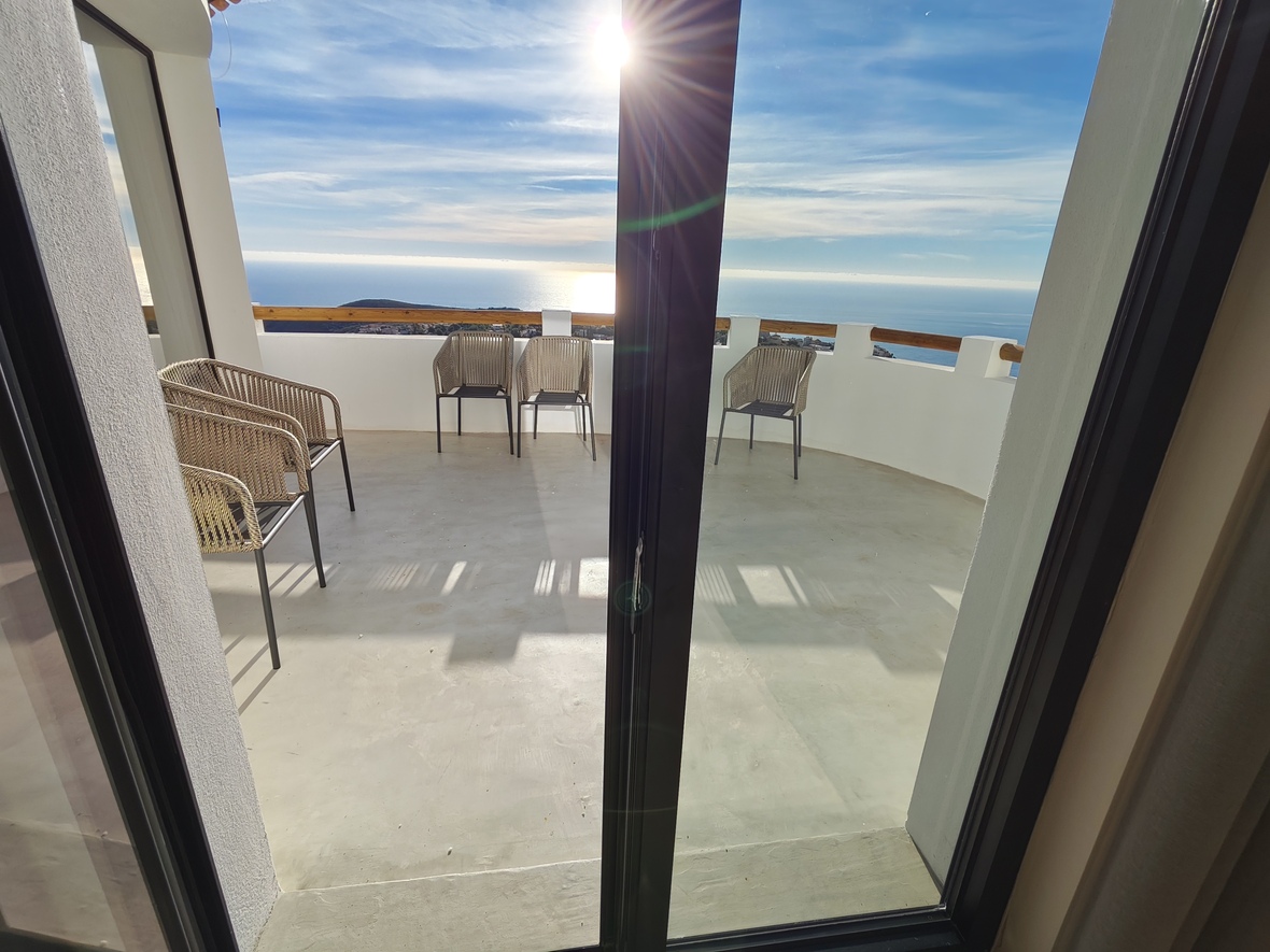 Terrasse mit Panoramablick auf das Meer, ausgestattet mit geflochtenen Stühlen, weißen Mauern mit Holzhandlauf und poliertem Betonboden.