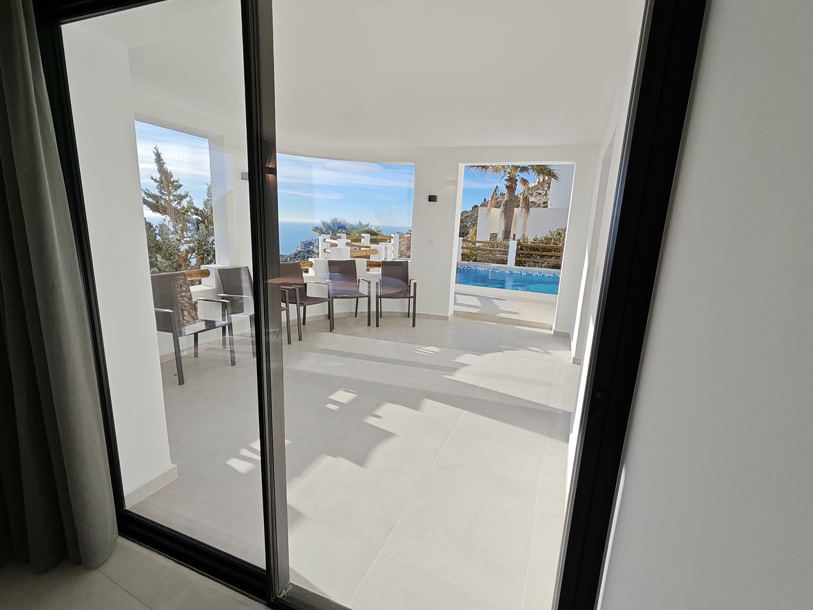 Überdachte Terrasse mit hellen Bodenfliesen und Außenmöbeln, die einen weiten Blick auf das Meer und den privaten Poolbereich bietet.