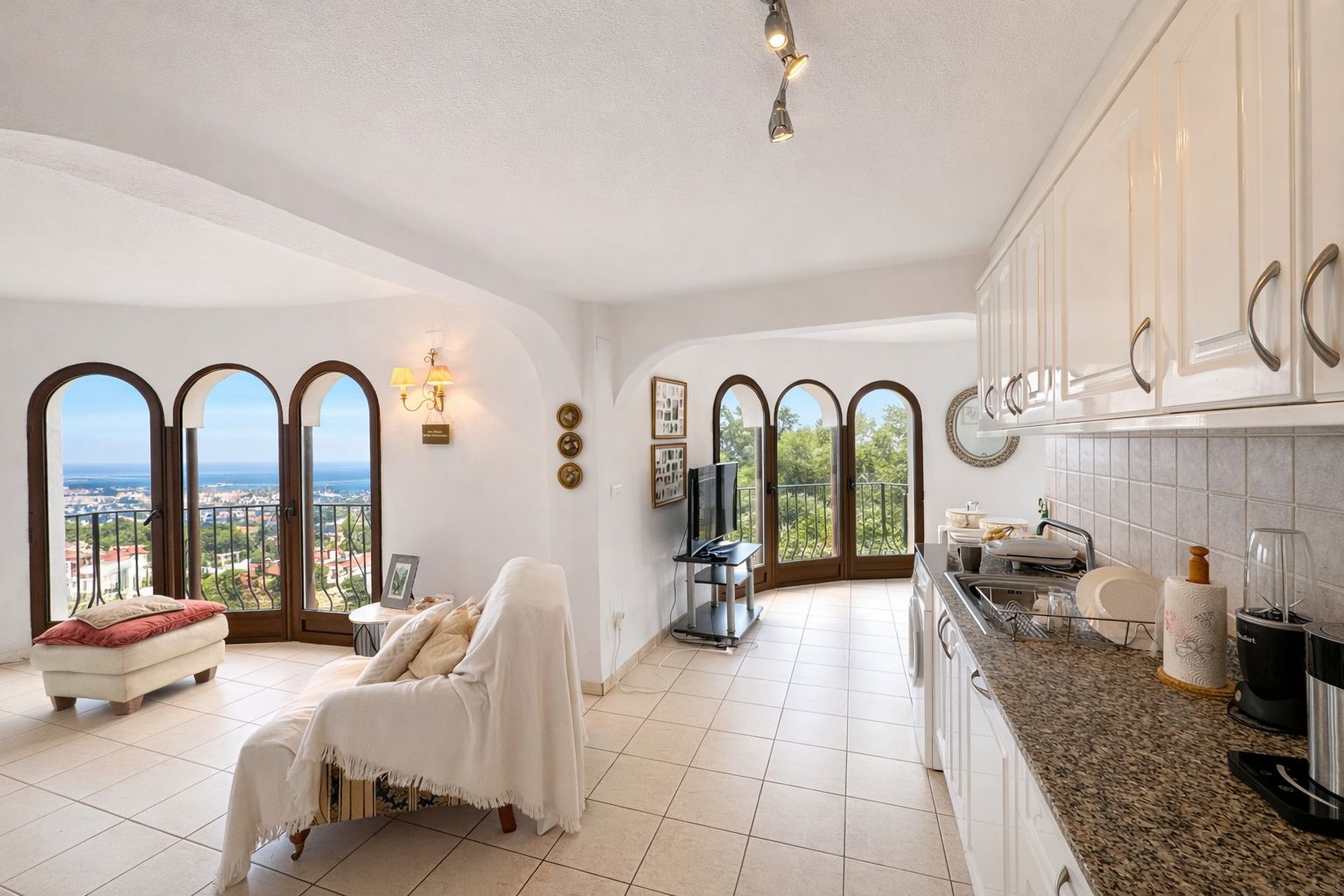 Offener Wohnbereich mit Einbauküche, Arbeitsplatten aus Granit und Rundbogenfenstern, die einen Panoramablick auf das Meer und die Küste bieten.