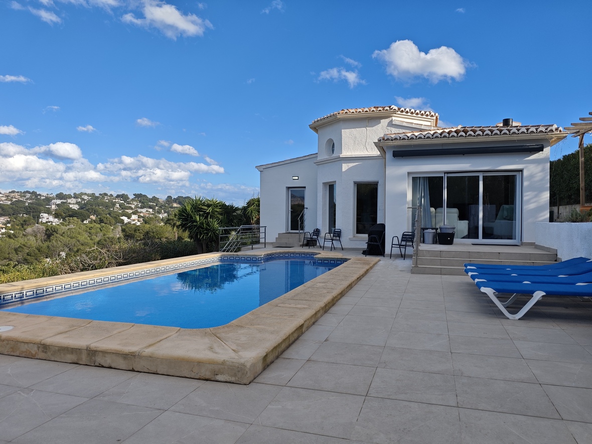 Außen-Terrasse mit rechteckigem Pool, Steineinfassung, blauen Sonnenliegen und Blick auf die umliegenden Hügel und Landschaft.