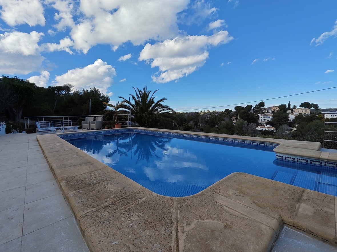 Außenpool mit blauen Mosaikfliesen und Steineinfassung, mit Blick auf die umliegende mediterrane Landschaft und die Wohngegend.