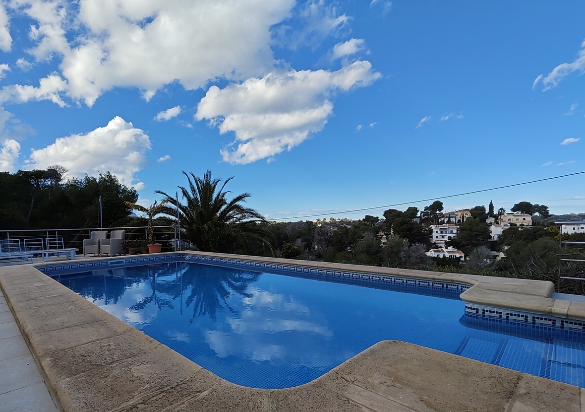 Außenpool mit blauen Mosaikfliesen und Steineinfassung, mit Blick auf die umliegende mediterrane Wohngegend und üppige Vegetation.
