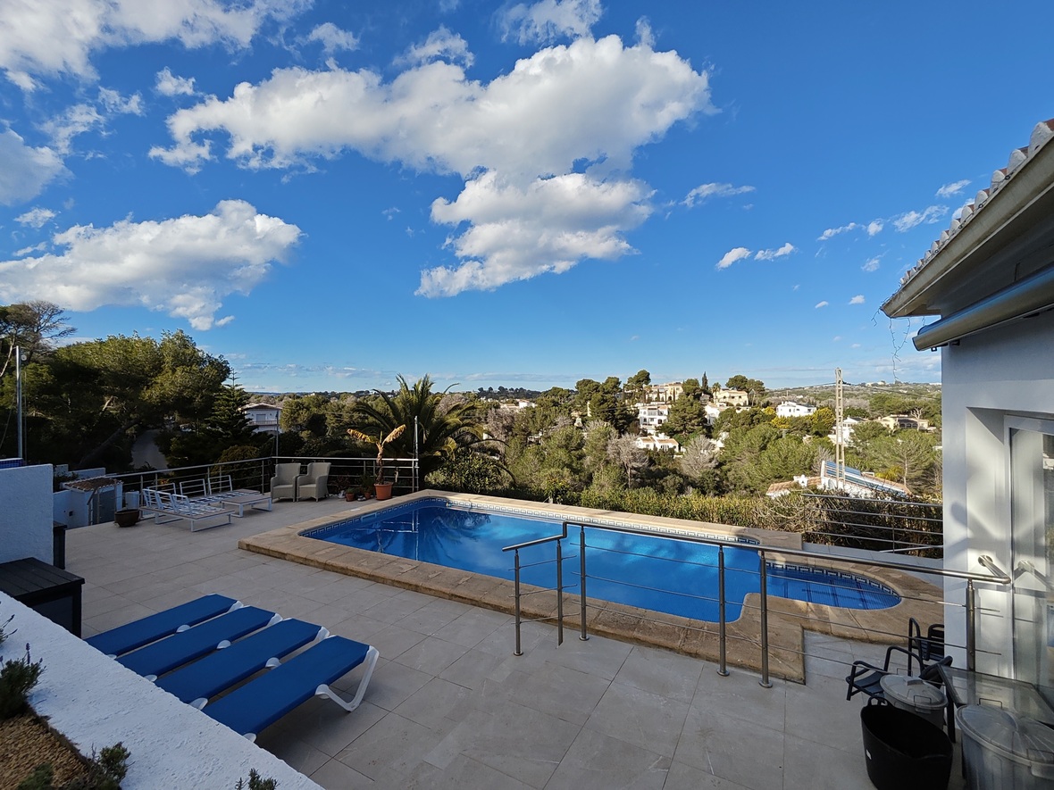Erhöhte Terrasse mit rechteckigem Pool, blauen Sonnenliegen und Edelstahlgeländer mit weitem Blick über das bewaldete Wohngebiet.