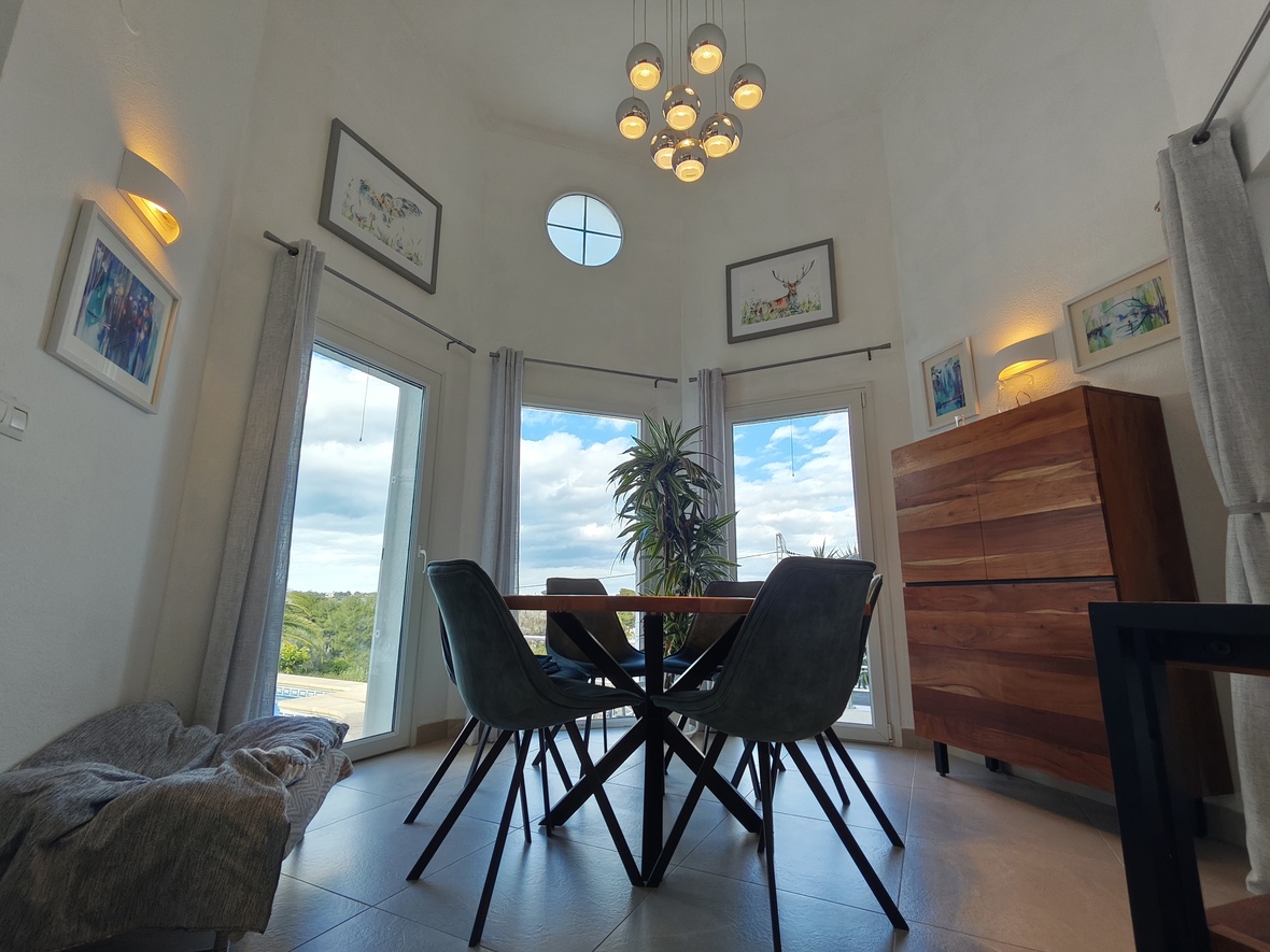 Esszimmer mit hohen Decken, moderner Kugel-Pendelleuchte und rundem Oberlicht. Ein Massivholz-Sideboard und große Glasfronten prägen den hellen, offenen Raum.