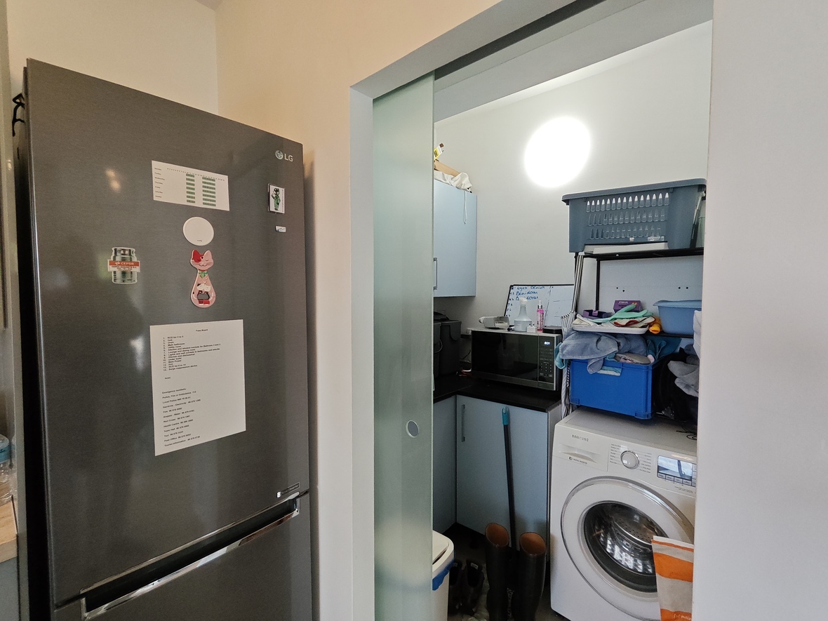 Hauswirtschaftsraum mit Milchglas-Schiebetür, ausgestattet mit Samsung-Waschmaschine, Mikrowelle und hellblauen Schränken neben einem LG-Kühlschrank.