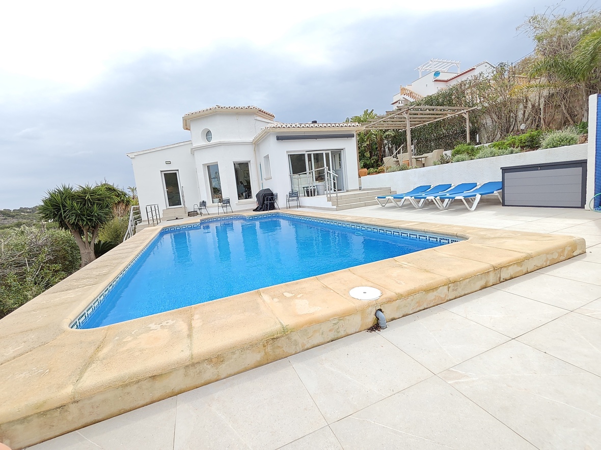 Privater rechteckiger Pool mit blauen Fliesen und Steineinfassung, umgeben von einer hellen Fliesenterrasse mit Sonnenliegen und einer weißen mediterranen Villa.