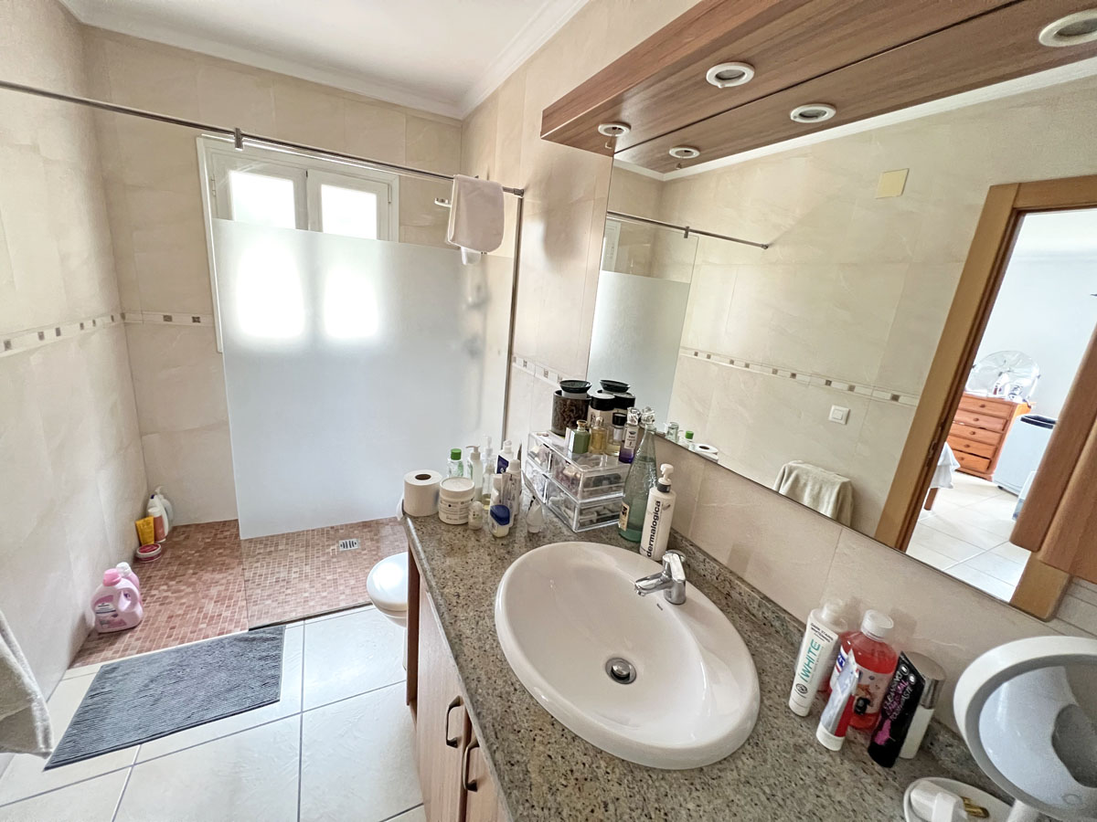 Badezimmer mit Granit-Arbeitsplatte, ovalem Waschbecken und integrierter Spiegelbeleuchtung. Begehbare Dusche mit Milchglastrennung und Mosaikboden.