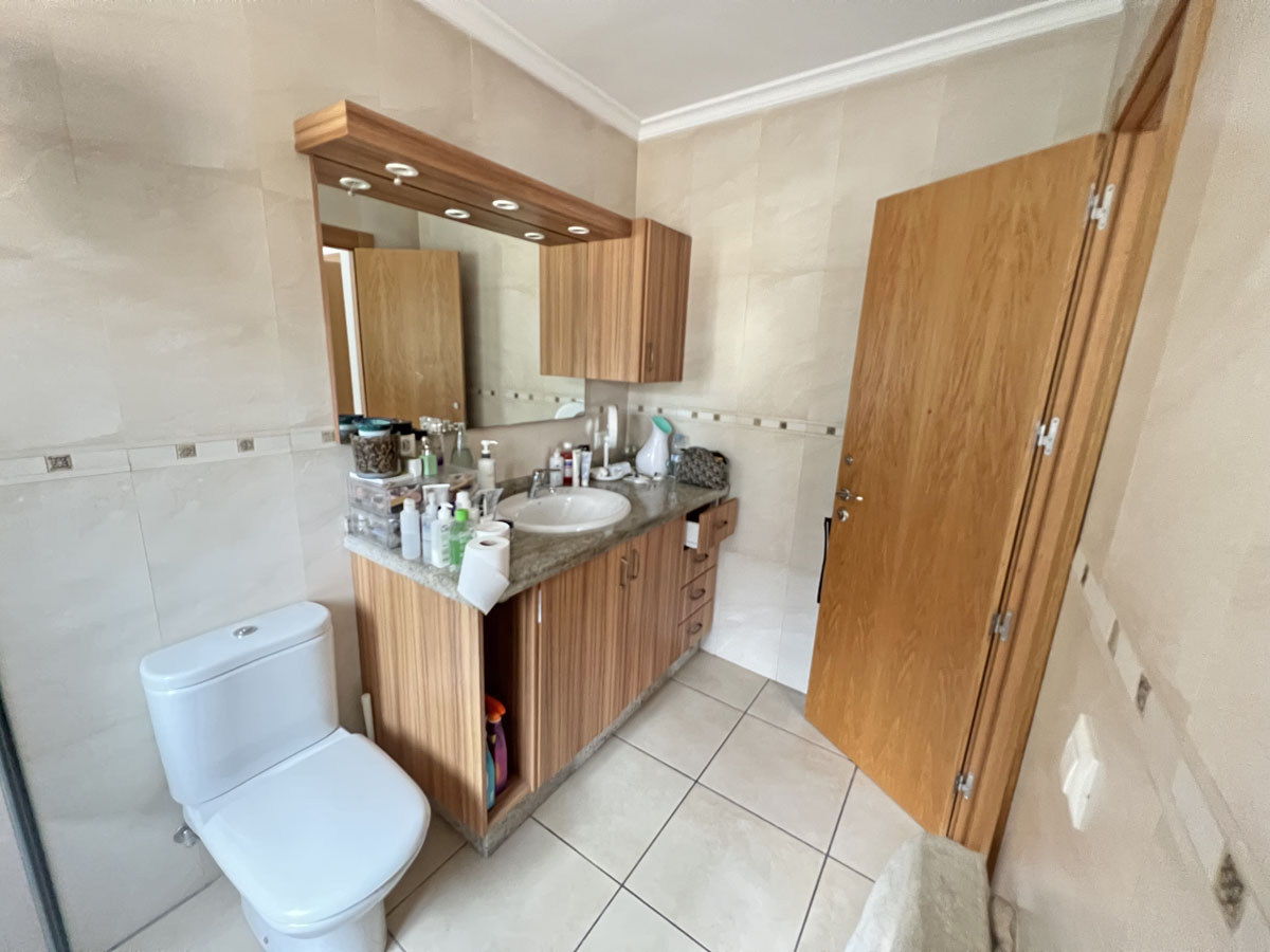 Badezimmer mit Holz-Waschtisch, Granit-Arbeitsplatte und Spiegel mit integrierter Beleuchtung. Cremefarbene Wandfliesen mit dekorativer Bordüre.