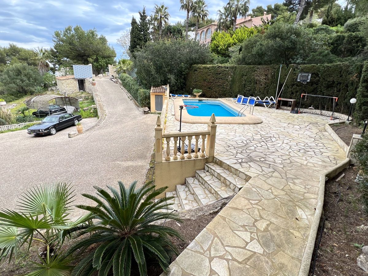 Erhöhte Terrasse mit Natursteinpflaster, privatem Pool und einer großzügigen Einfahrt mit Parkplatz, umgeben von mediterraner Vegetation.