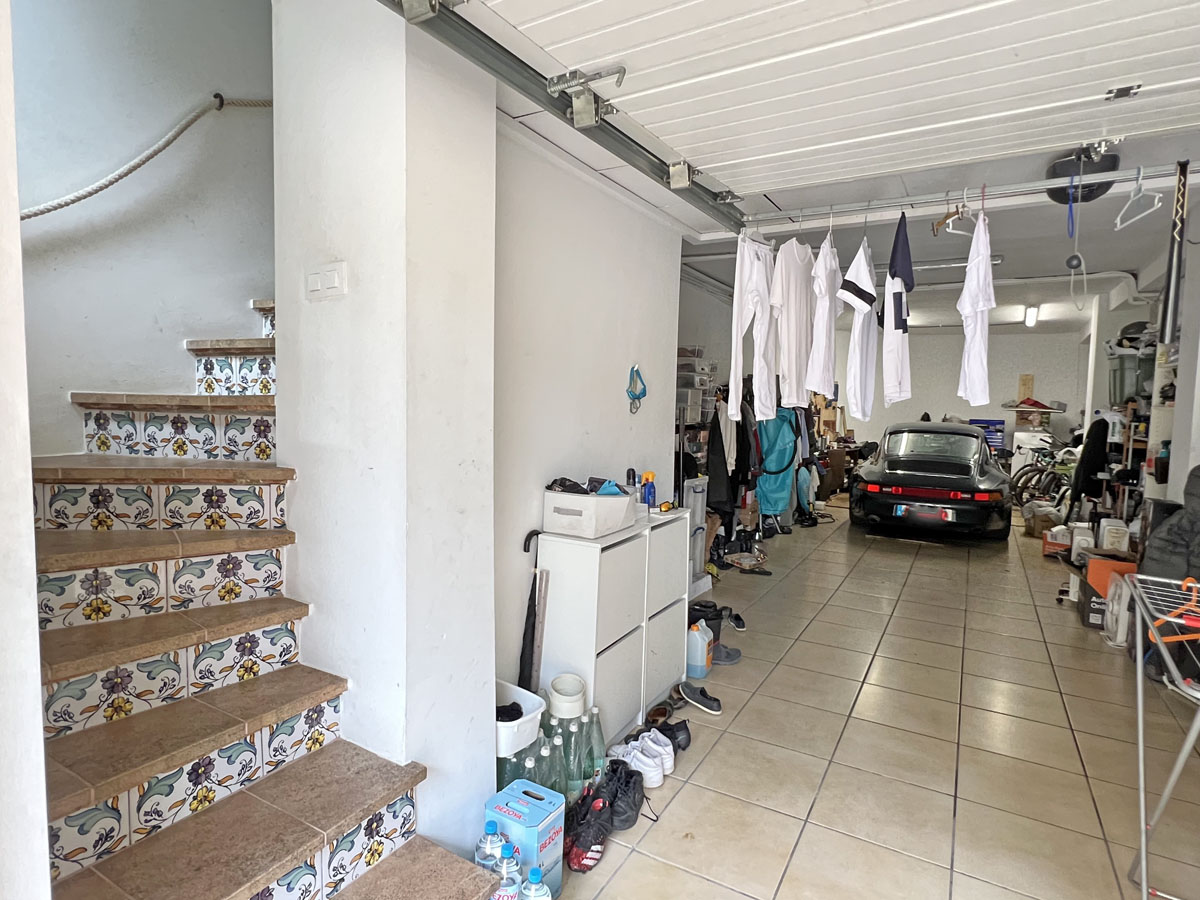 Geräumige Garage mit Fliesenboden und direktem Innenzugang über eine Treppe mit traditionellen mediterranen Dekorkacheln.