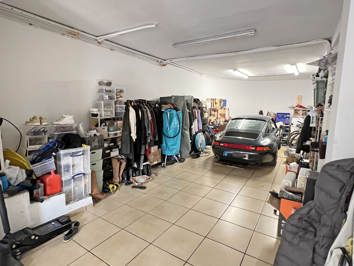 Große Garage mit Keramikfliesenboden, Leuchtstoffröhrenbeleuchtung sowie mehreren Regalen und Ständern für eine organisierte Lagerung.