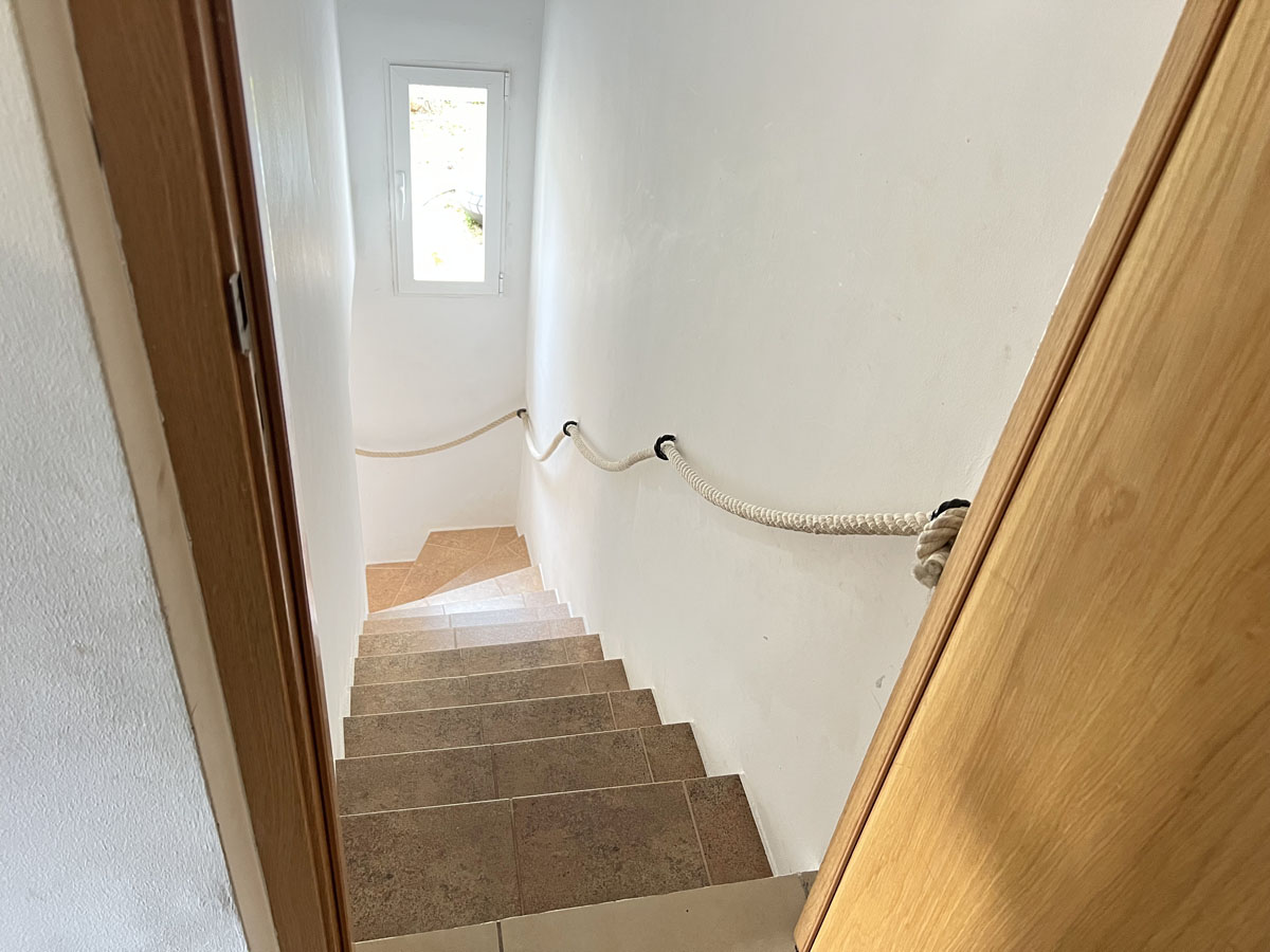 Innentreppe mit Keramikstufen und einem markanten Seilhandlauf, die durch ein Fenster am Treppenabsatz mit Tageslicht versorgt wird.