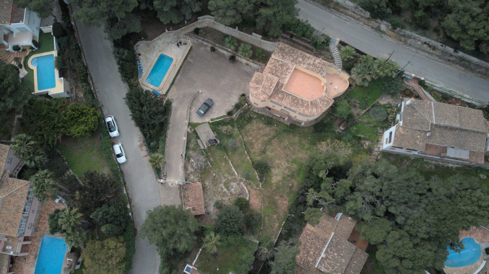 Luftaufnahme der Immobilie mit Darstellung des Grundstückslayouts, des rechteckigen Pools, der großzügigen Parkfläche und des terrassierten Gartens.