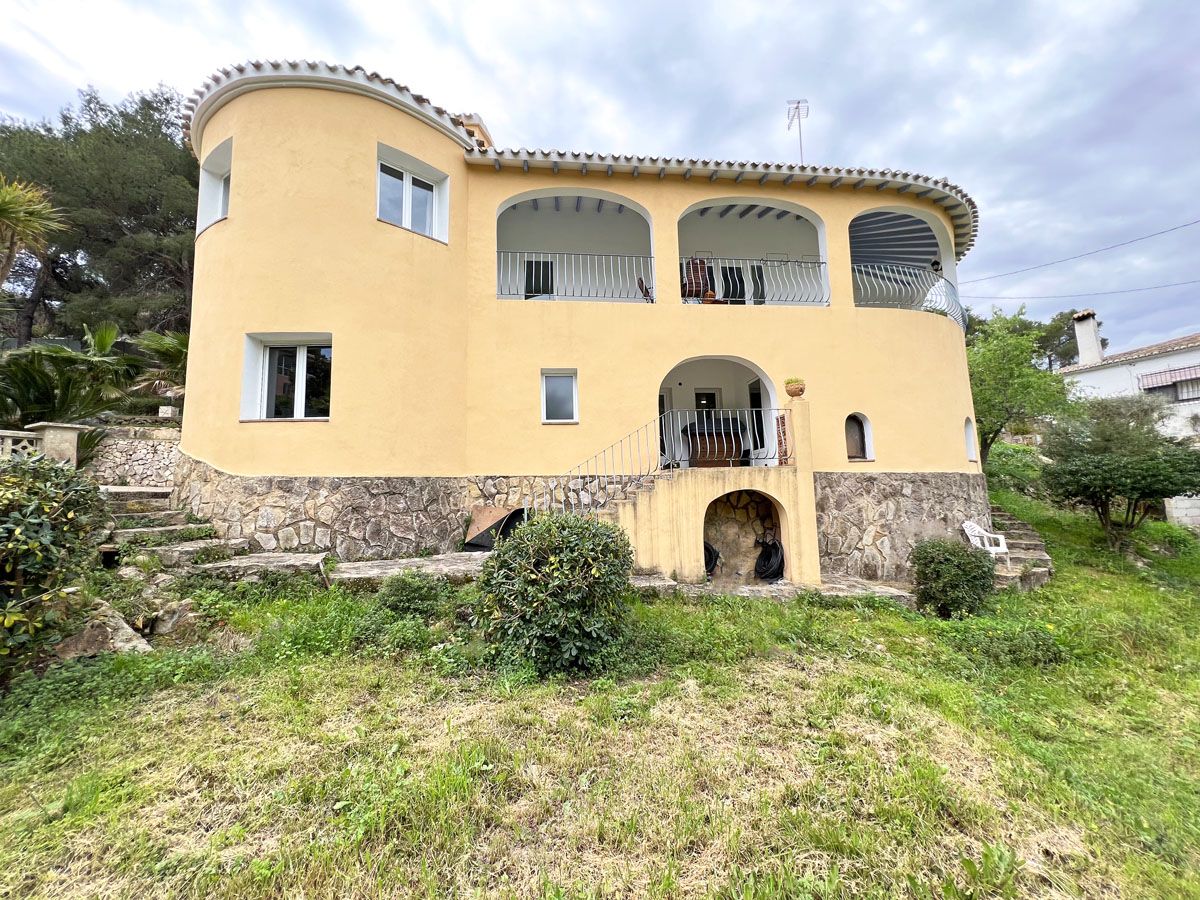 Mediterrane Außenansicht mit geschwungener gelber Fassade, Natursteinsockel, Bogenterrassen im Obergeschoss und einem terrassierten Gartenbereich.