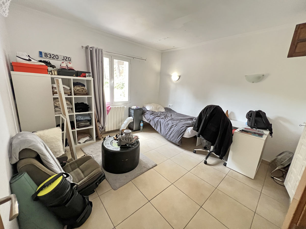 Schlafzimmer im separaten Studio mit hellen Bodenfliesen, weißen Wänden und Tageslicht. Der Raum bietet Platz für einen Arbeitsbereich und Regalsysteme.