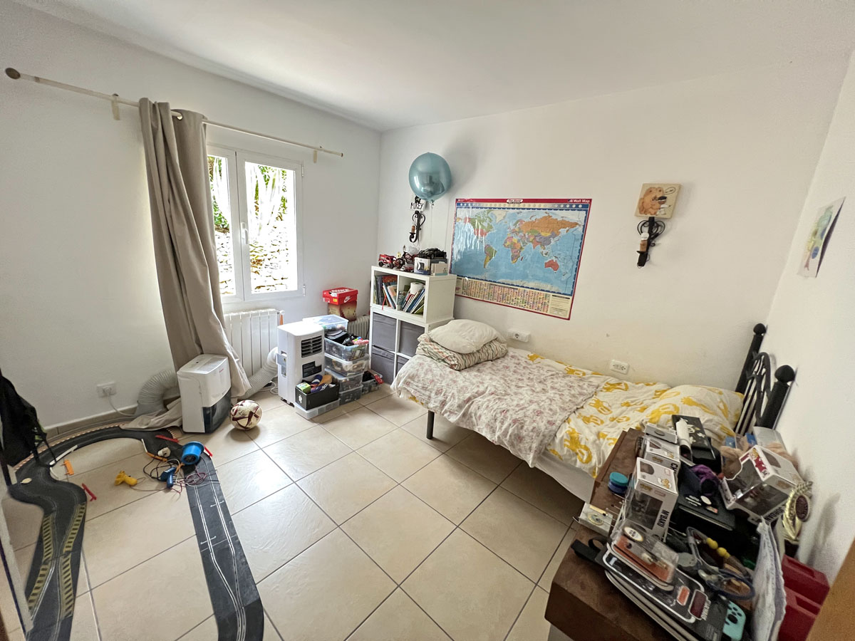 Schlafzimmer mit Fliesenboden, Heizkörper und Fenster für natürliches Licht. Der Raum verfügt über weiße Wände und eine funktionale Aufteilung.