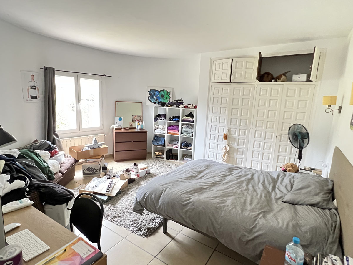 Schlafzimmer mit großen weißen Einbauschränken im Paneel-Design, Fliesenboden und einem Fenster für natürliches Tageslicht.
