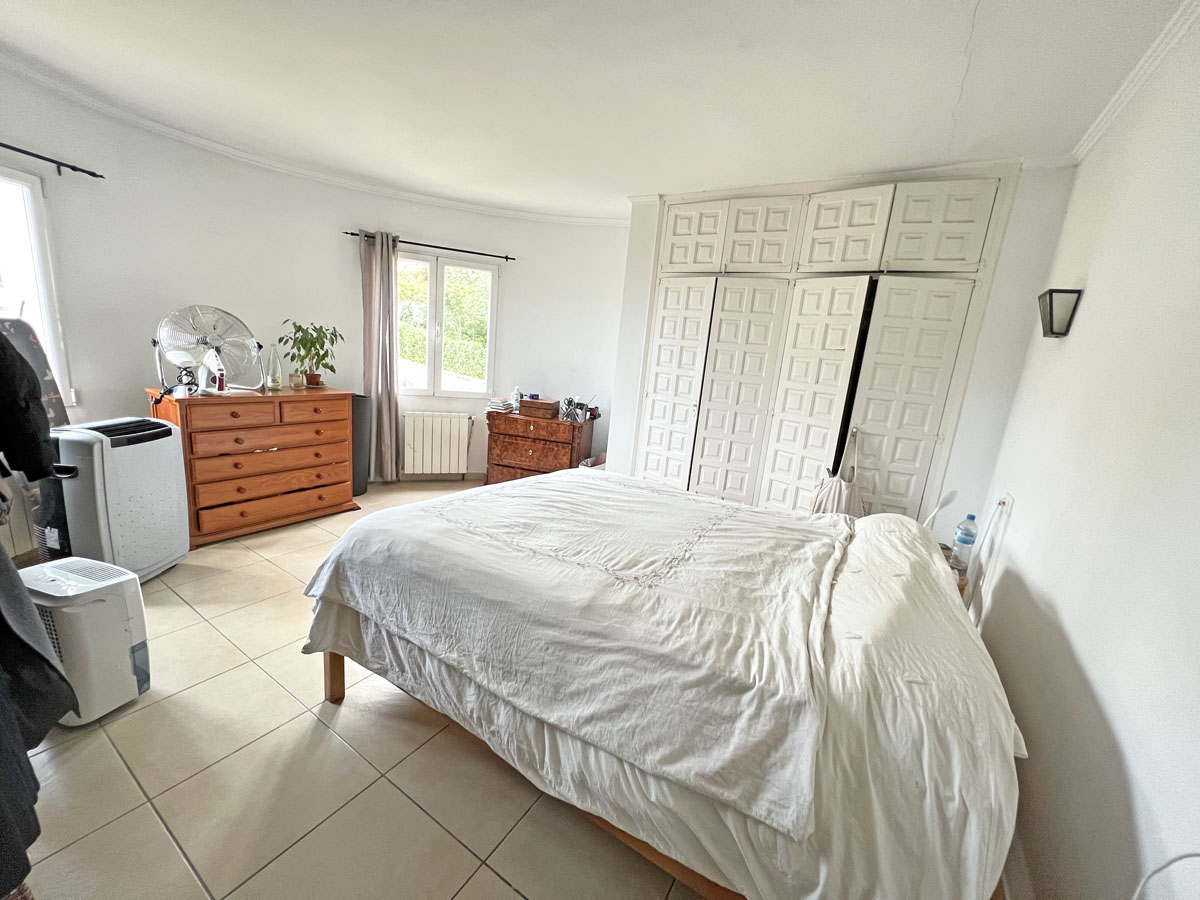 Schlafzimmer mit großzügigen Einbauschränken im Paneel-Design, Fliesenboden und Tageslicht durch das seitliche Fenster.