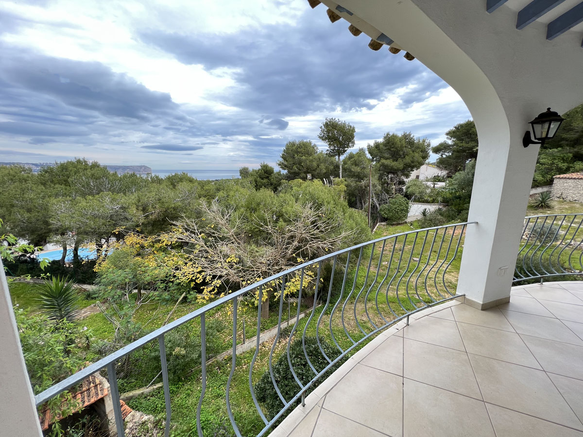 Überdachte Terrasse mit Rundbögen und Fliesenboden, die einen weiten Blick auf das Mittelmeer und das Cabo San Antonio über Pinienbäume bietet.