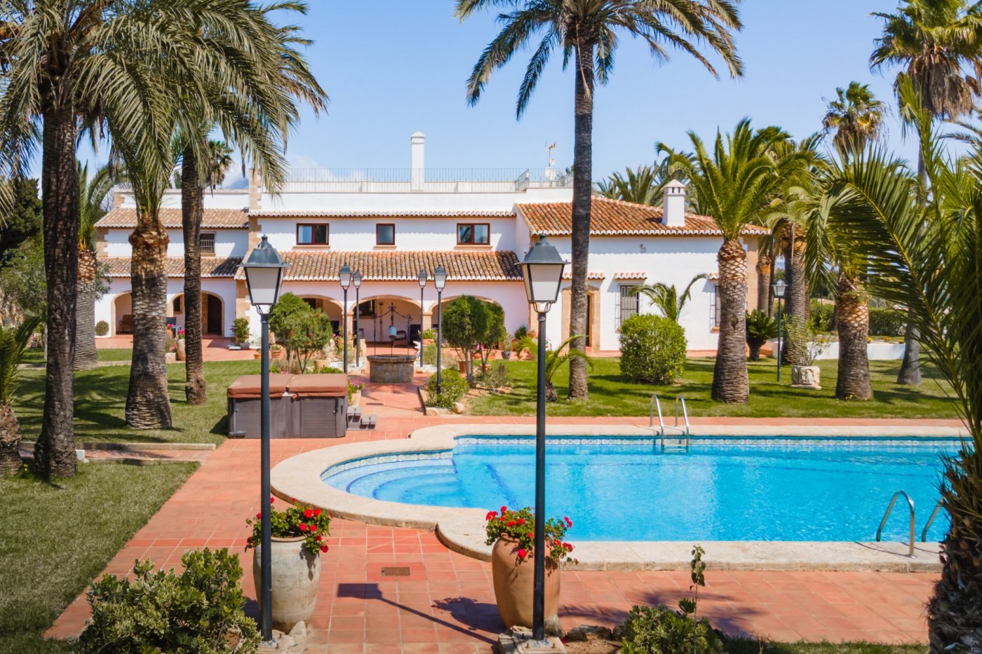 Außenansicht der mediterranen Villa mit Swimmingpool, gepflegtem Garten mit Palmen und einer weitläufigen Terrakotta-Terrasse mit dekorativen Laternen.
