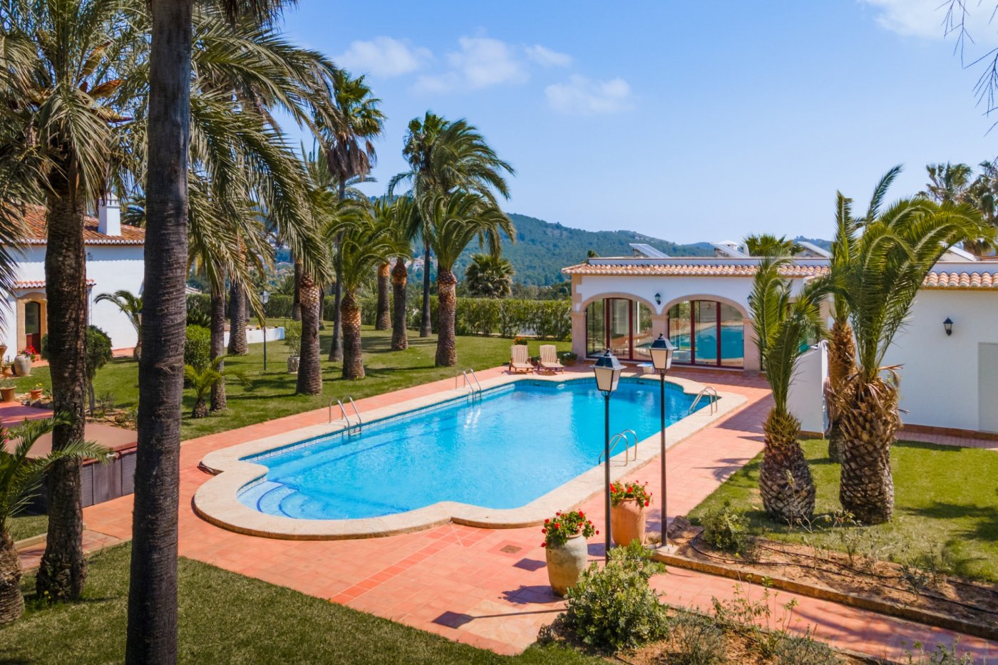 Großer 16x7m Pool mit Terrakotta-Terrasse, umgeben von einem weitläufigen Palmengarten und einem Gästehaus mit traditionellen Rundbögen.