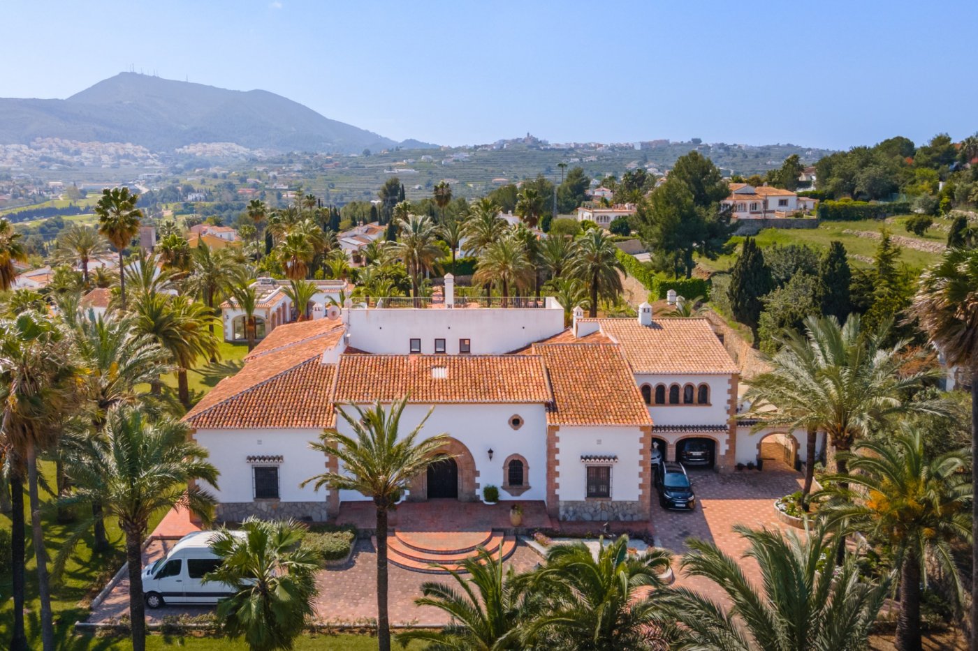 Luftaufnahme der mediterranen Villa mit Terrakotta-Ziegeldächern, Tosca-Steinbögen und einem weitläufigen, von Palmen gesäumten Grundstück mit Talblick.