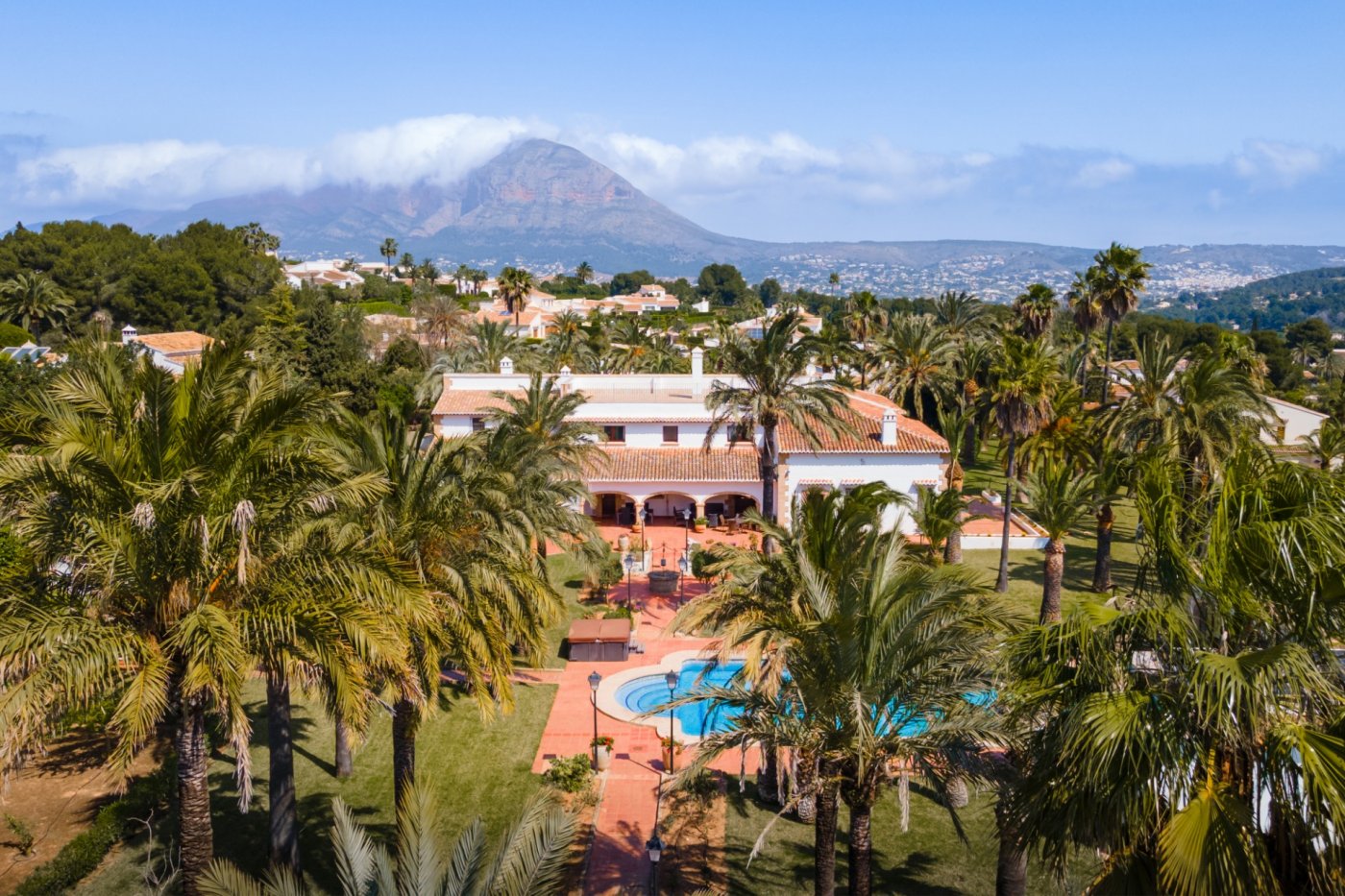 Luftaufnahme der mediterranen Villa mit weitläufigem Palmengarten, privatem Pool und Panoramablick auf den Berg Montgó im Hintergrund.