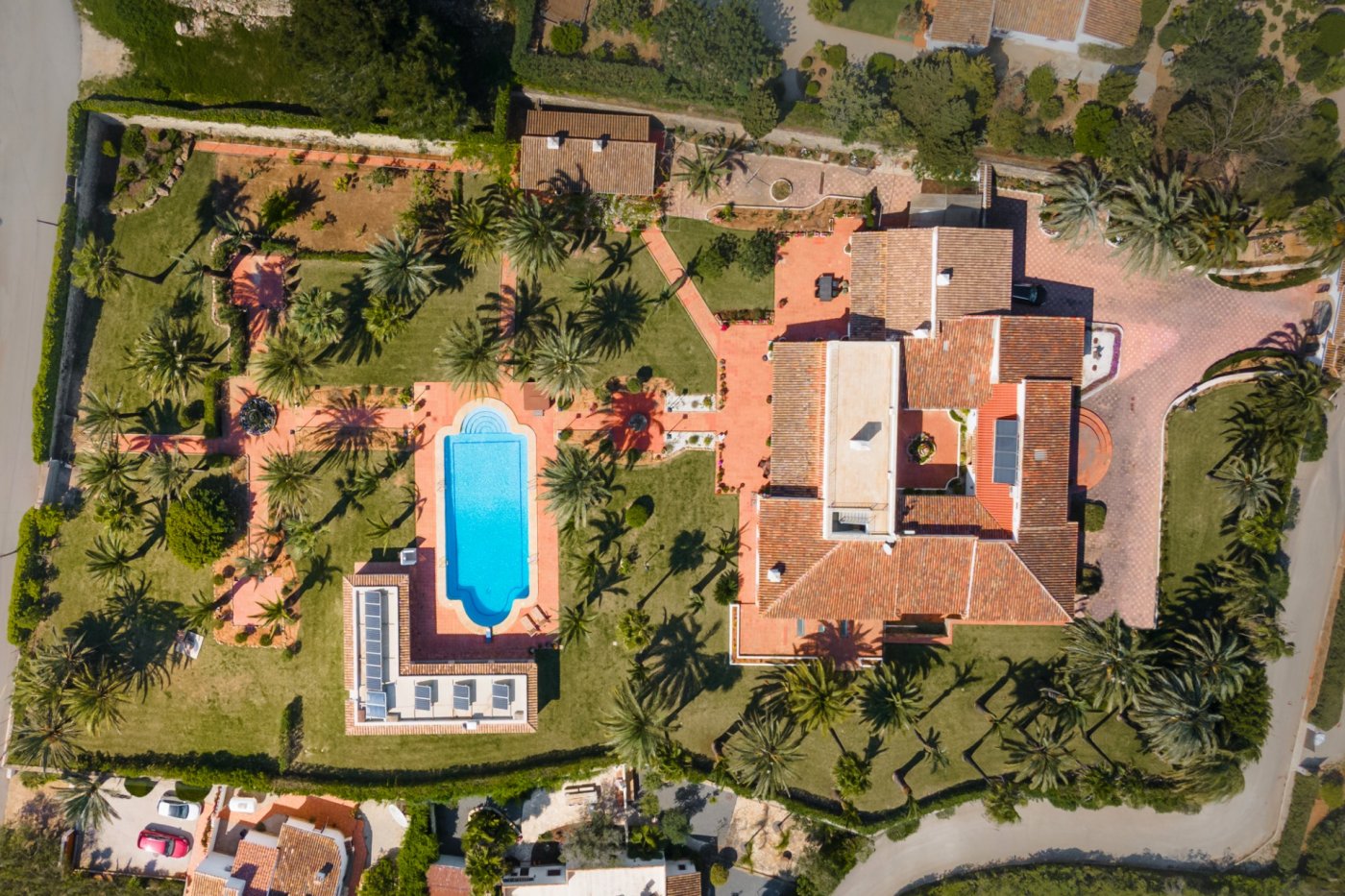 Luftaufnahme des Anwesens, die das Haupthaus mit Innenhof, den großen Pool und den weitläufigen, mit Palmen bepflanzten Garten zeigt.