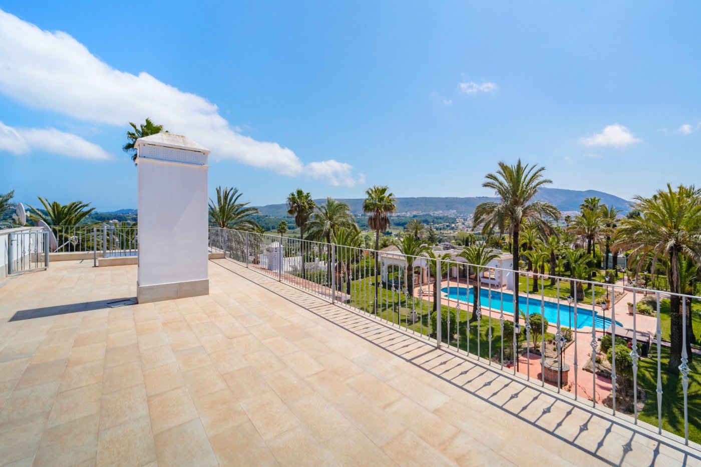 Obere Terrasse mit Fliesenboden und Metallgeländer, die einen weiten Blick über den Palmengarten, den großen Pool und das umliegende Tal bietet.