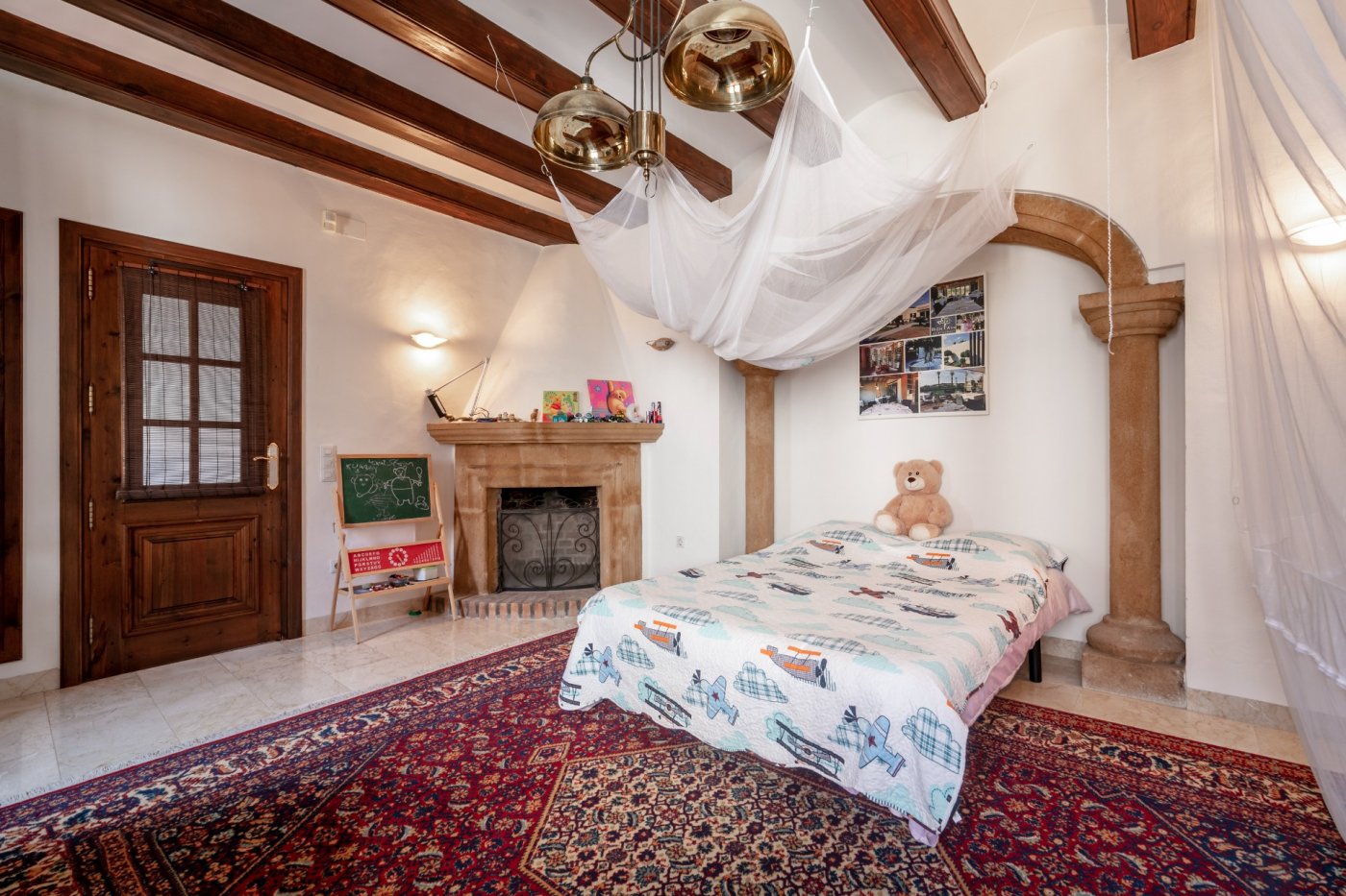 Schlafzimmer mit Holzbalkendecke, traditionellem Steinkamin und einem Rundbogen aus Tosca-Stein auf klassischen Säulen.
