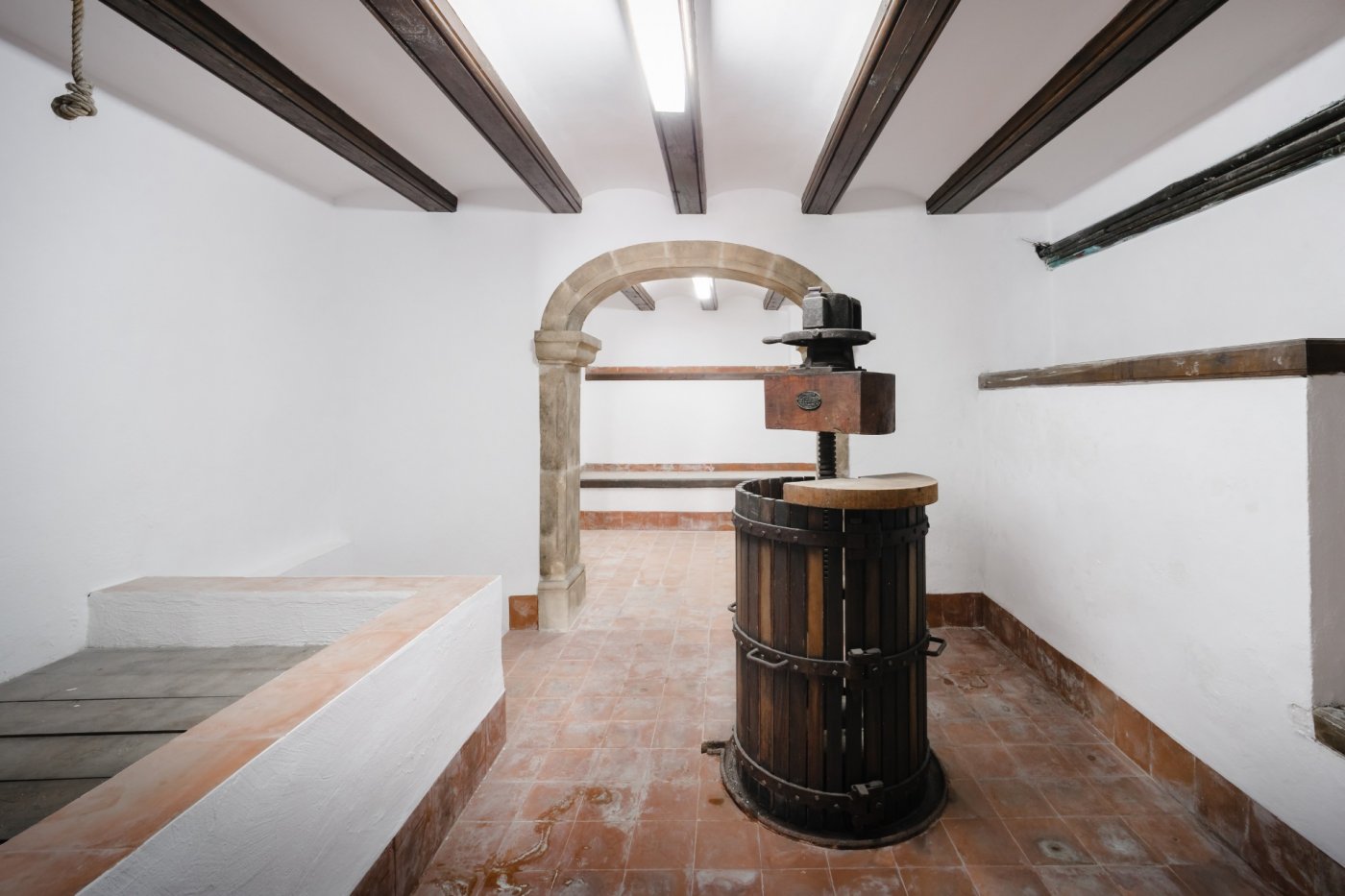 Traditioneller Weinkeller mit hölzerner Weinpresse, Terrakottaboden, dunklen Deckenbalken und einem originalen Rundbogen aus Tosca-Stein.