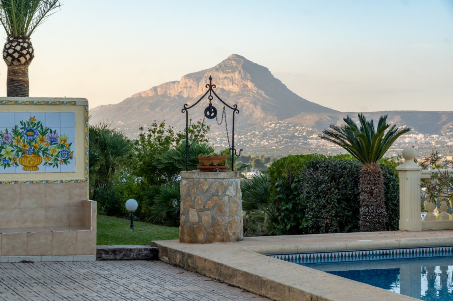 Blick vom Poolbereich mit dekorativem Steinbrunnen und traditionellem Keramikmosaik auf das Cabo San Antonio und die umliegende Landschaft von Jávea.