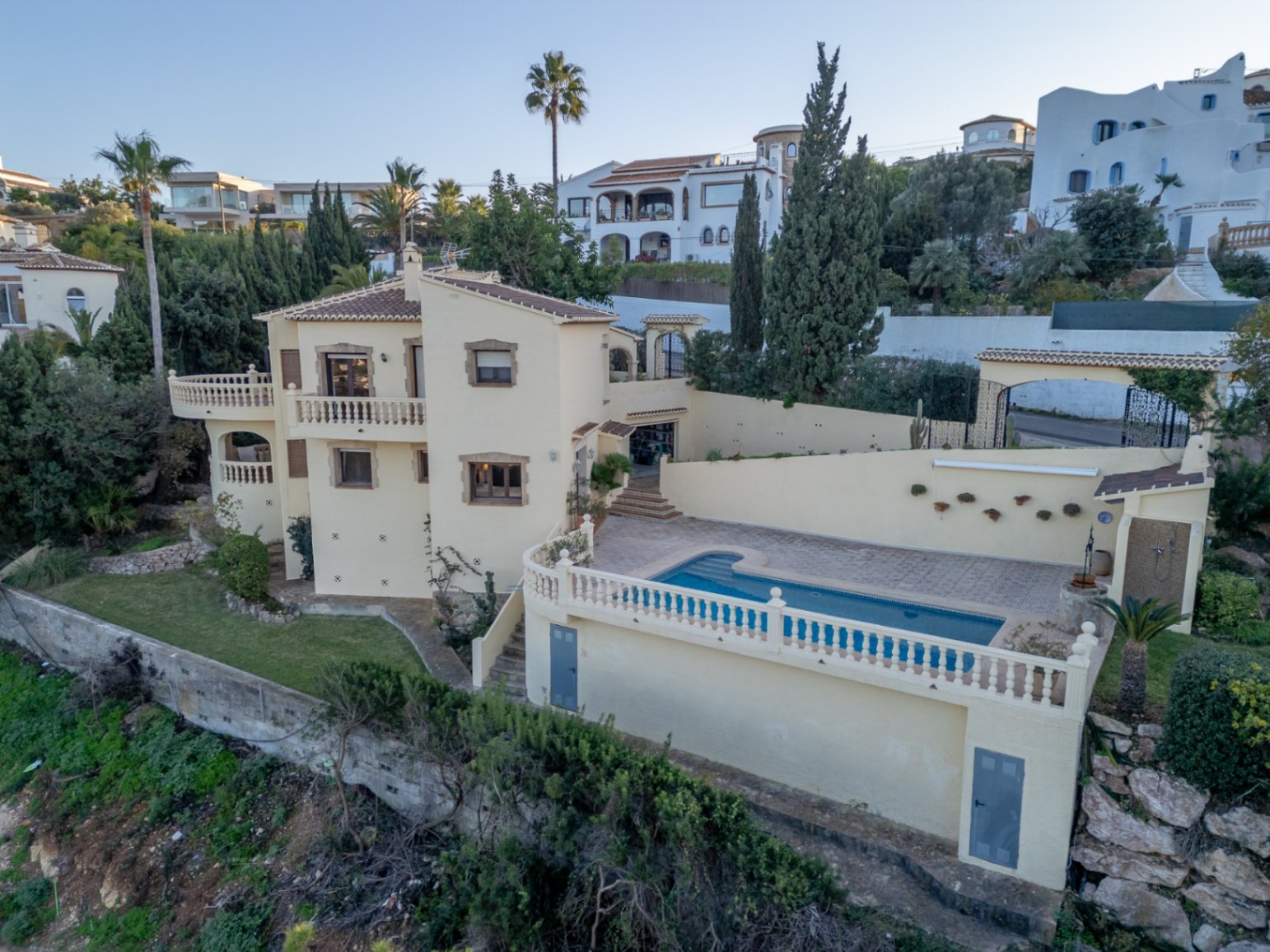 Erhöhte Außenansicht der mediterranen Villa mit privatem Pool, Terrassen mit weißen Balustraden und Fensterfassungen aus Naturstein.