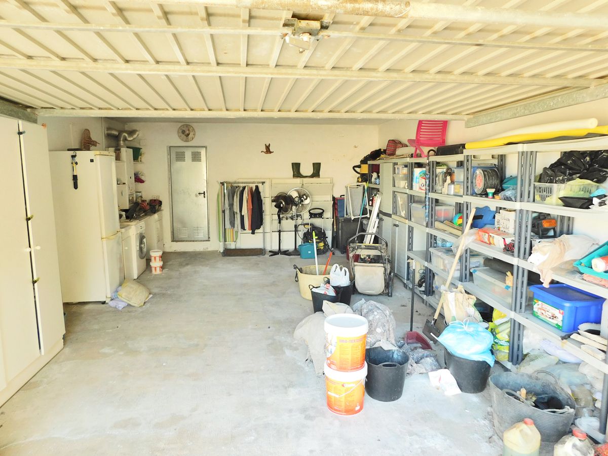 Geräumige Garage mit Betonboden, Metallregalen für Stauraum und einem Hauswirtschaftsbereich mit Waschmaschine und zusätzlichem Kühlschrank.