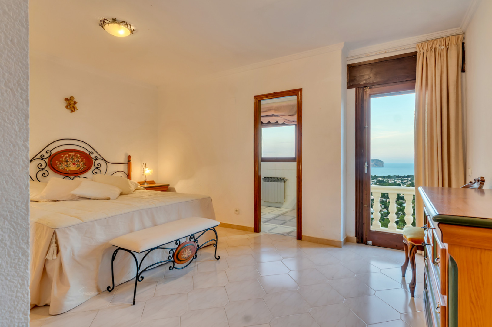 Hauptschlafzimmer mit kunstvollem Schmiedeeisen-Bettgestell, Fliesenboden und direktem Zugang zum Balkon mit Blick auf das Meer und das Cabo San Antonio.
