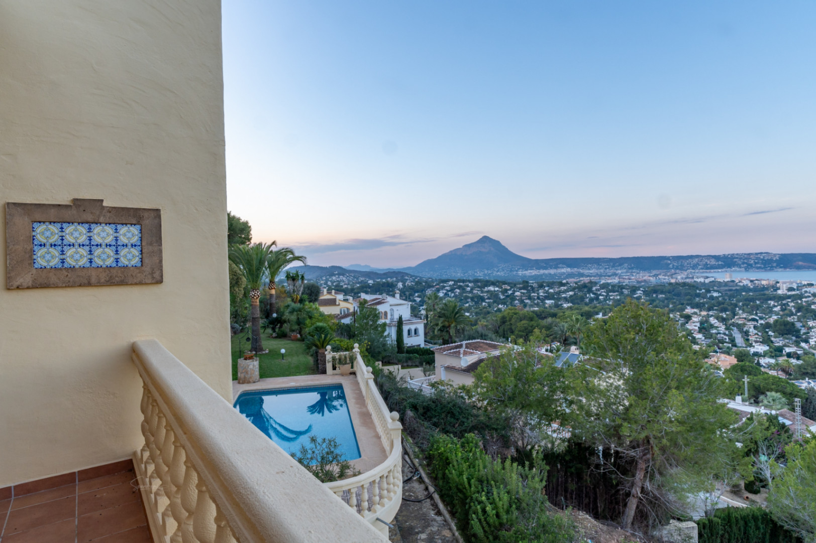 Obere Terrasse mit Steinbalustrade und dekorativem Fliesenelement, Blick auf den privaten Pool, den mediterranen Garten und das Panorama des Montgó über der Bucht von Jávea.