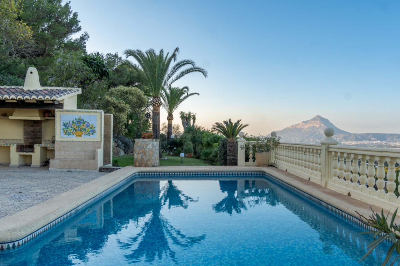 Rechteckiger Mosaikpool mit überdachter Außenküche und Keramikdekor, eingebettet in einen mediterranen Garten mit Blick auf den Montgó.