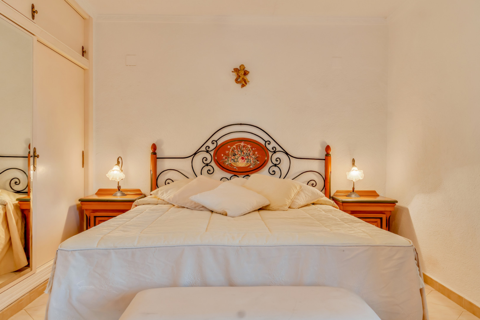 Schlafzimmer mit Doppelbett, dekorativem schmiedeeisernem Kopfteil, passenden Nachttischen aus Holz und Einbauschrank mit Spiegelfront.