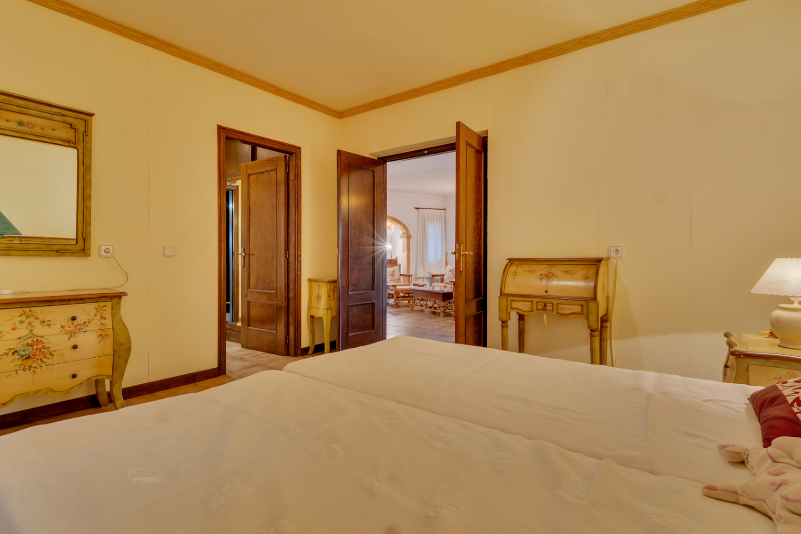 Schlafzimmer mit handbemalten klassischen Möbeln, Massivholztüren und Blick auf den Wohnbereich mit traditionellen Steinbögen.